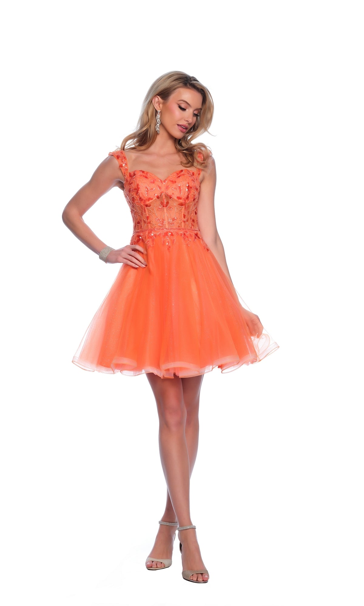 A woman models the Orange Homecoming Dress 12038, featuring floral embellishments and a tulle skirt, while wearing heels against a white background.